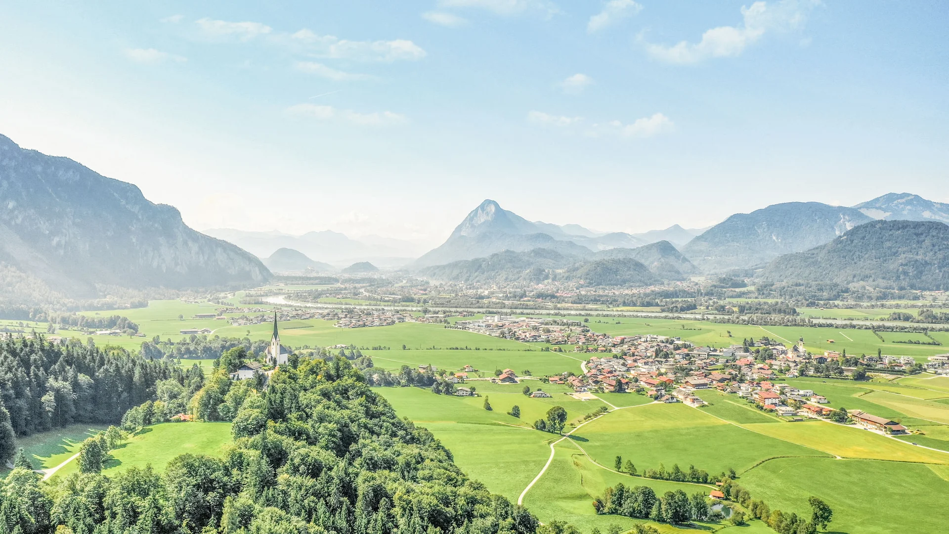Blick auf eine grüne Alpenlandschaft mit Bergen und einem Dorf