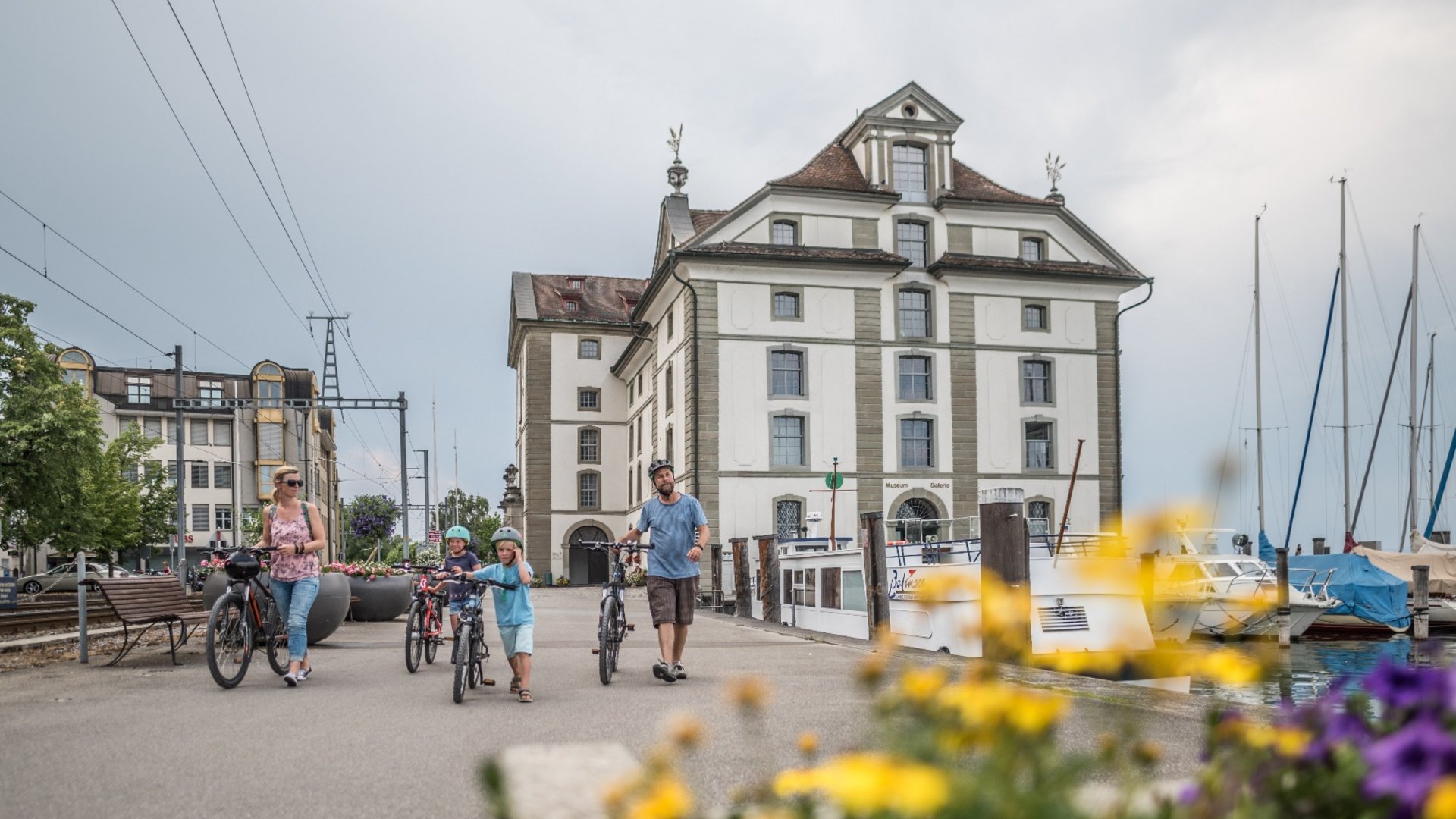 Family with bikes walking by lake harbor and historic building