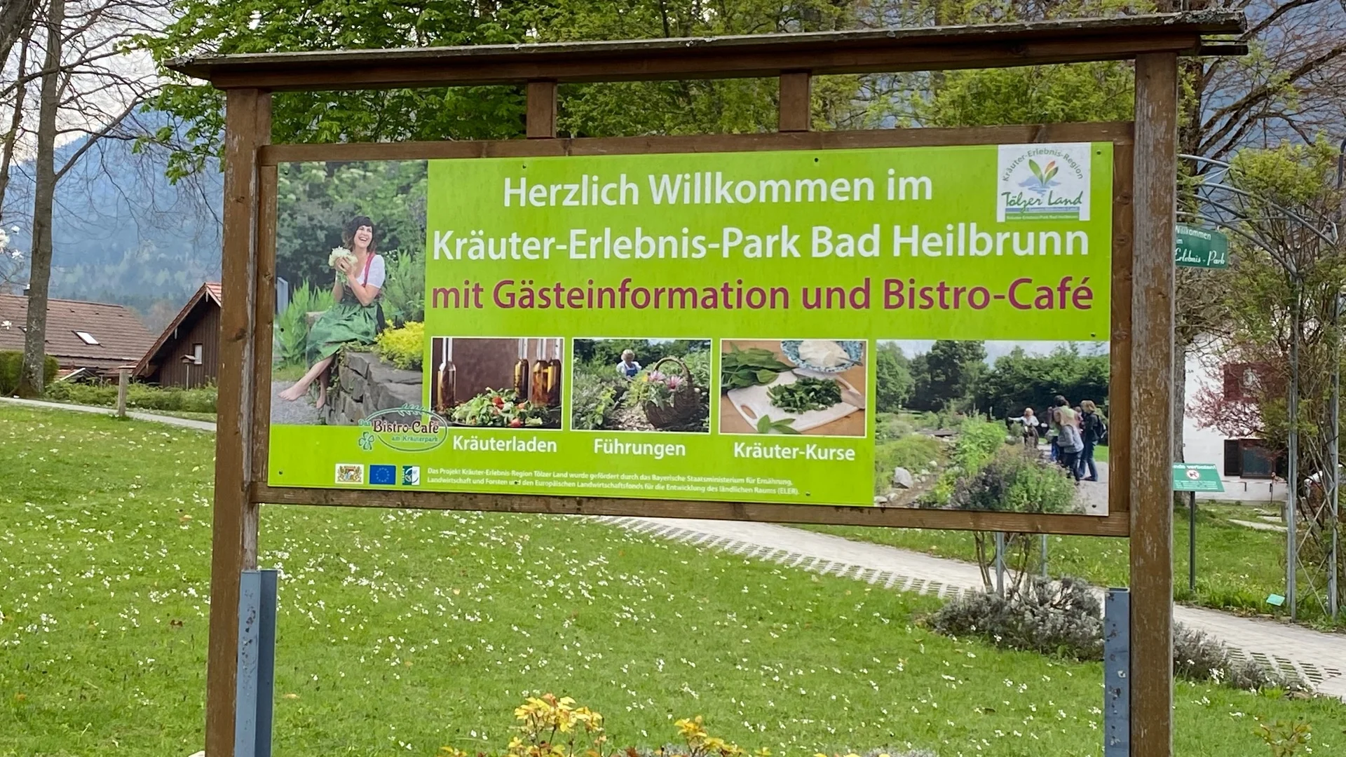 Schild mit Willkommen im Kräuter-Erlebnis-Park Bad Heilbrunn und Infos zum Bistro-Café