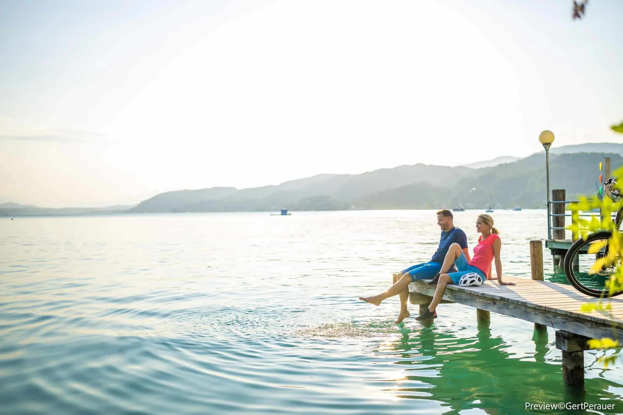 Paar sitzt auf Steg neben See, baumelt mit Füßen im Wasser