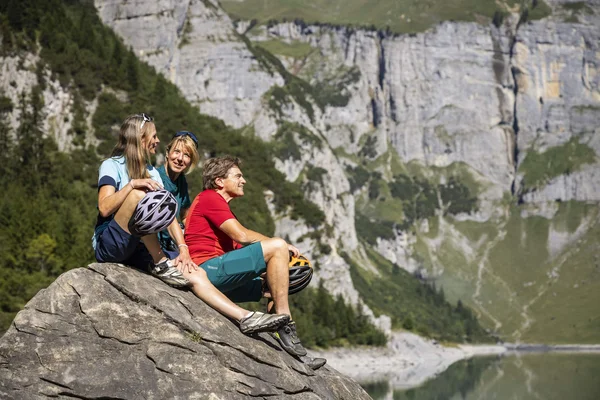Drei Personen mit Fahrrädern sitzen auf einem Felsen mit Bergblick