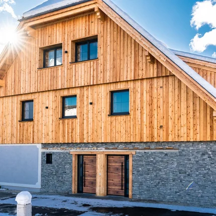 Haus mit Holzfassade und verschneitem Dach bei Sonnenschein