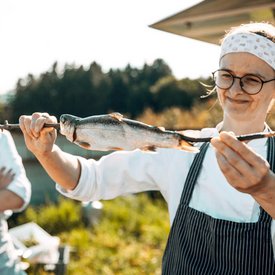 Woman holding smoked fish on a stick outdoors