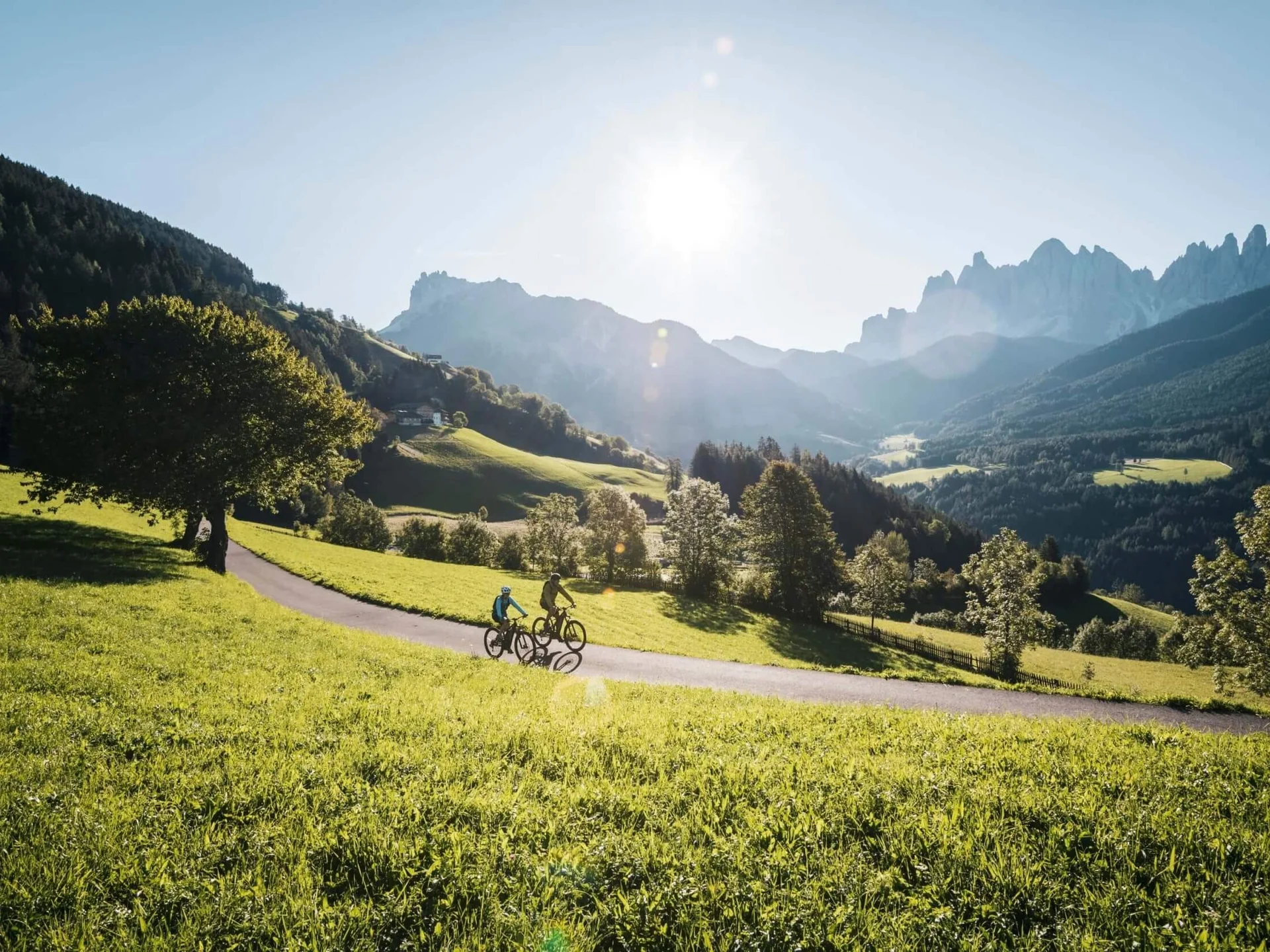 Zwei Radfahrer fahren auf einem Weg durch grüne Alpenlandschaft bei sonnigem Wetter