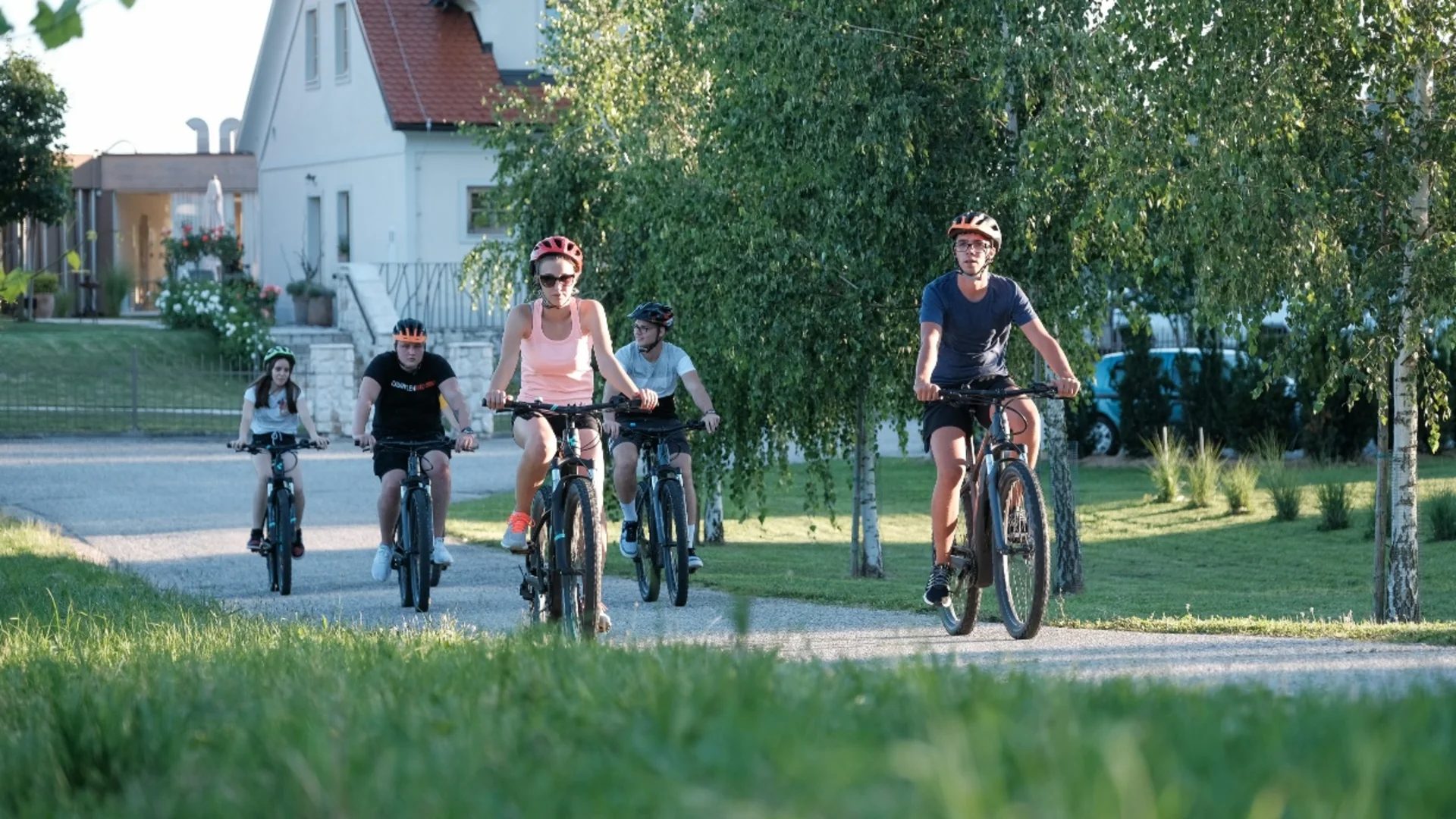 Vijf personen fietsen op een pad naast bomen en huizen.