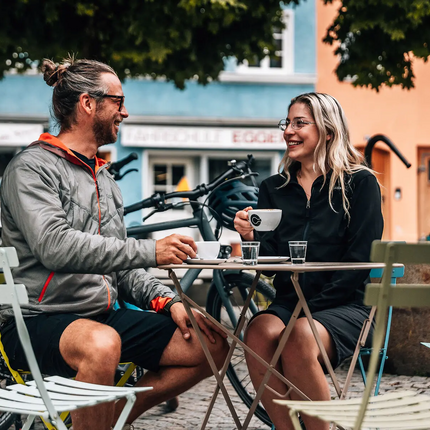 Two people enjoying coffee outdoors at a small table, smiling and talking