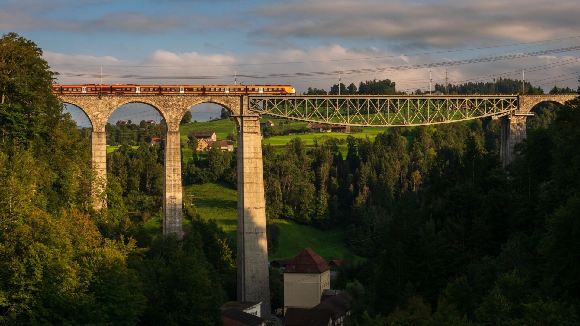 Train on a tall stone bridge over a forested valley at sunset