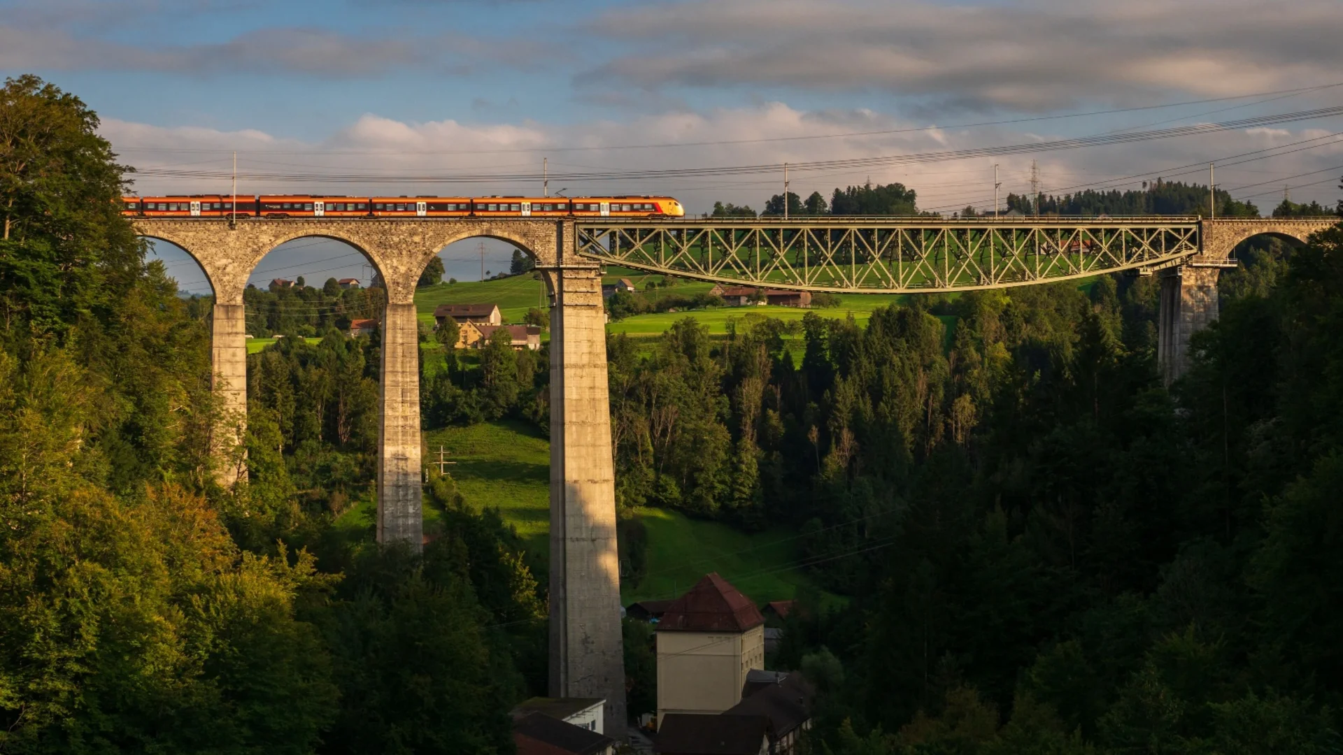 Zug auf einer hohen Steinbrücke über ein bewaldetes Tal bei Sonnenuntergang