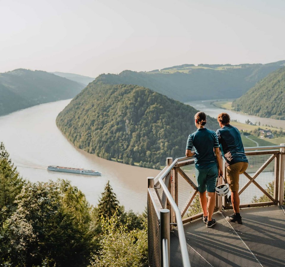 Zwei Personen auf Aussichtsplattform über Fluss und Bergen mit Schiff