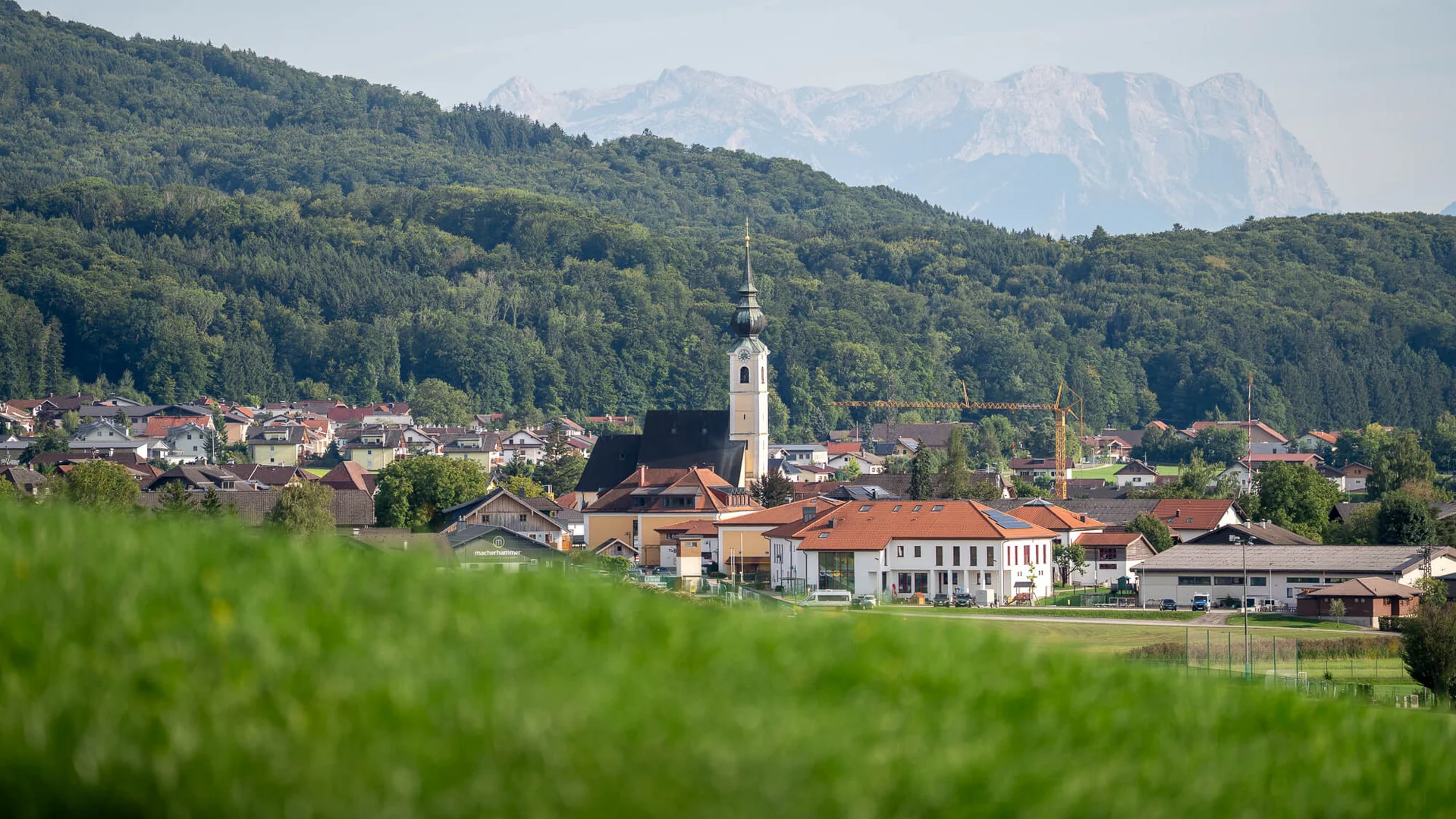 Haunsbergrunde © Jakob Eder Dorf mit Kirche vor bewaldeten Hügeln und Bergen im Hintergrund