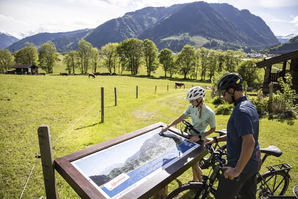 RadGENUSS im kleinen Juwel Maishofen © Velontour Zwei Radfahrer betrachten eine Panoramatafel vor Berglandschaft auf einer Wiese