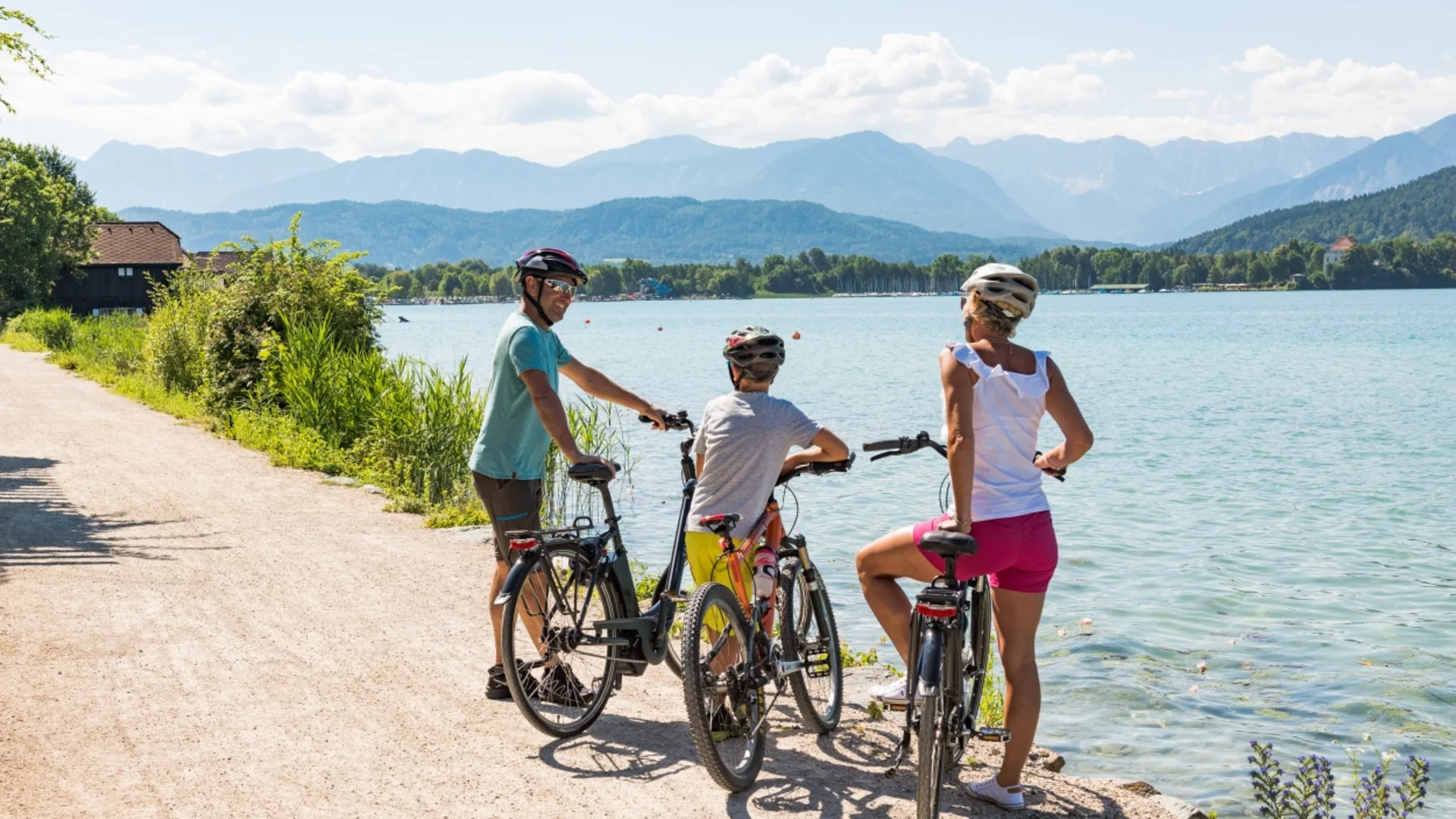 Drie fietsers met helmen bij een meer met bergen op de achtergrond