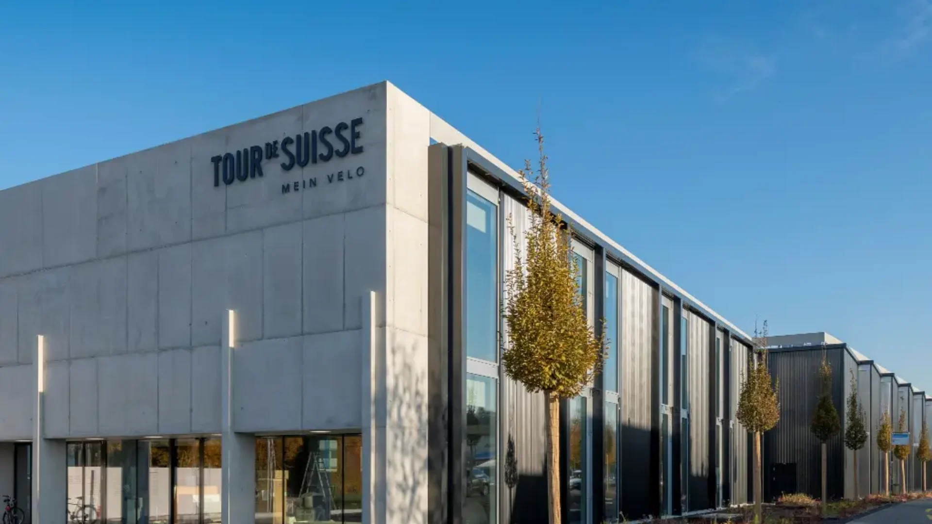 Modern gebouw met TOUR DE SUISSE MEIN VELO bord onder heldere hemel