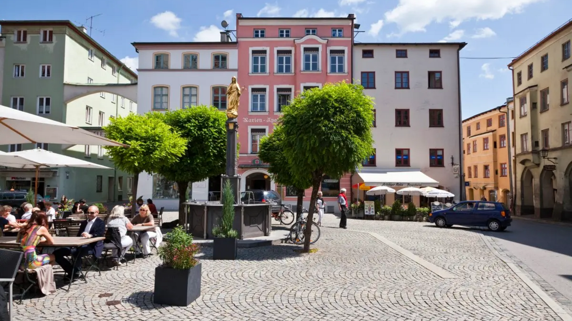 Busy square with cafes, trees, and colorful buildings under a blue sky