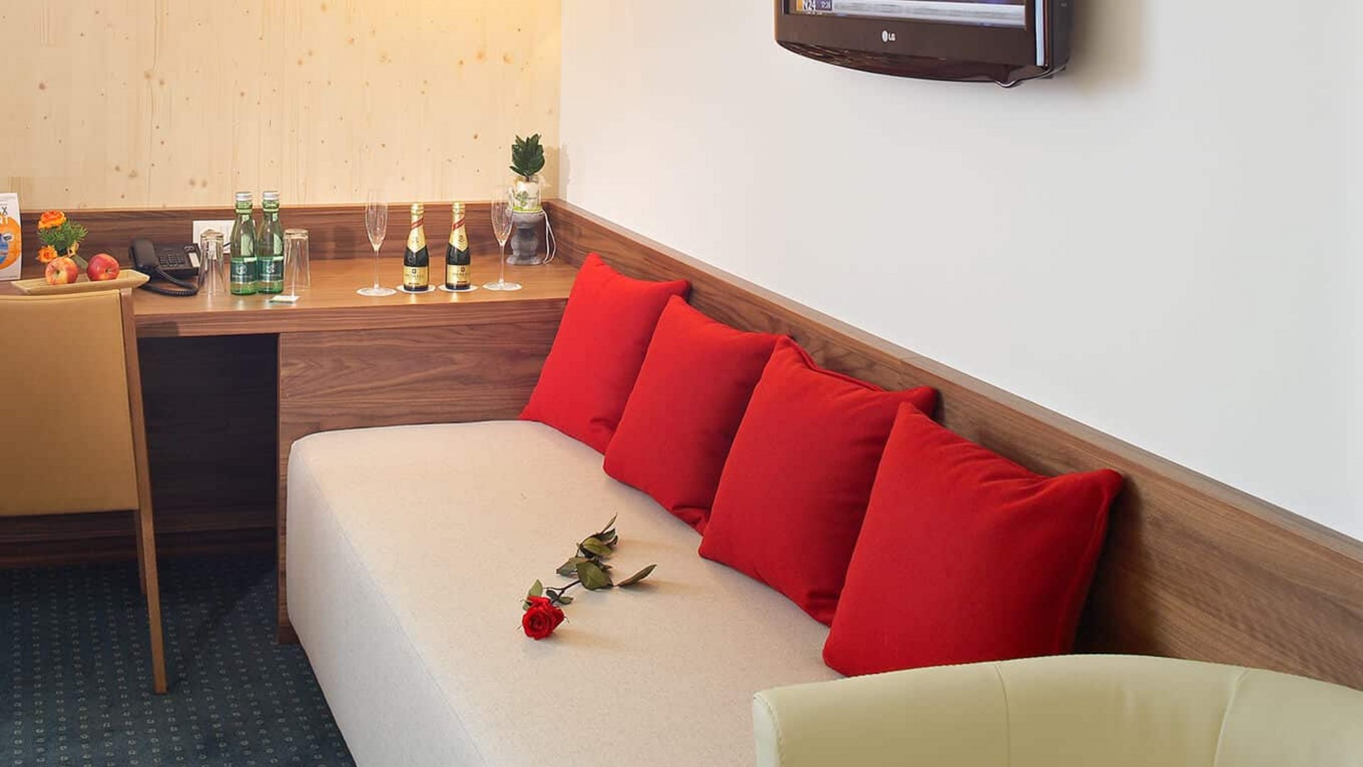 Hotel room with sofa, red cushions, TV, and a table with drinks