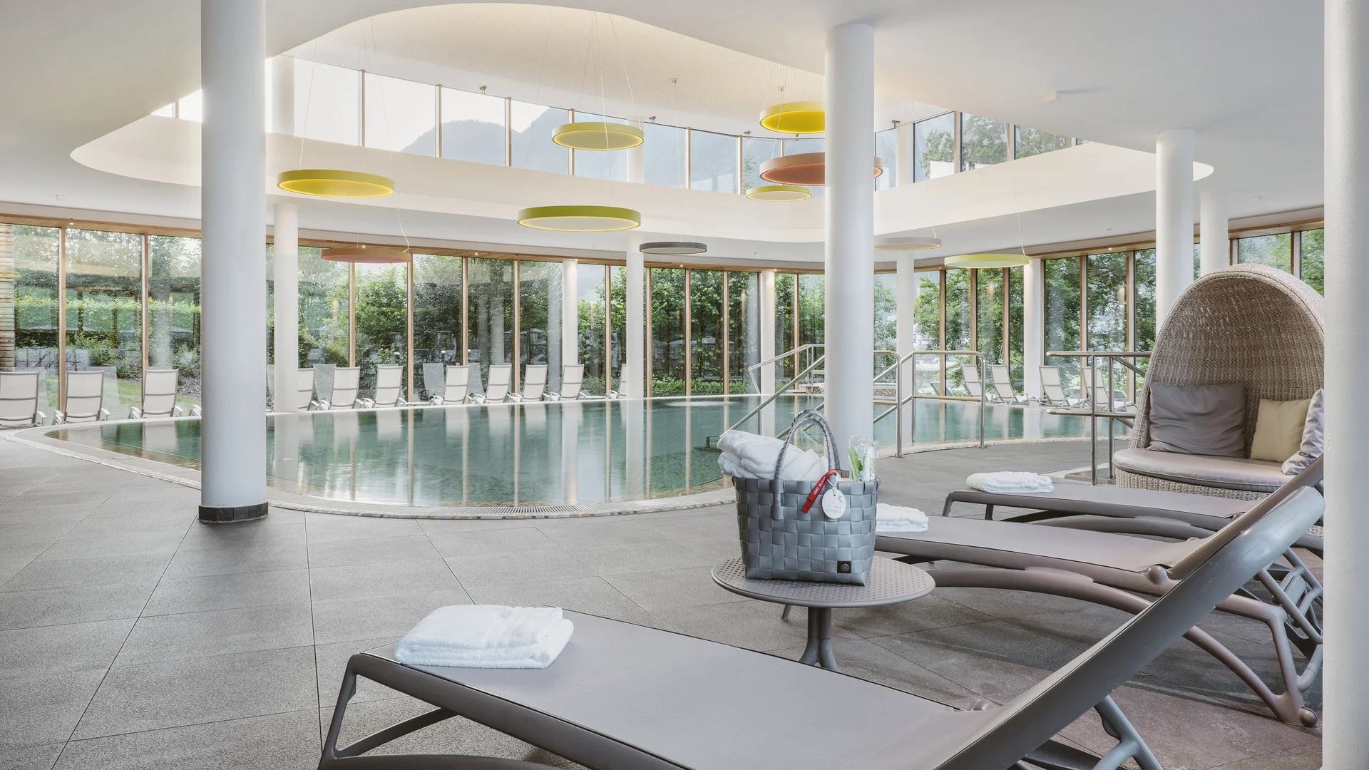 Innenpool mit Liegestühlen und großen Fenstern in modernem Wellnessbereich