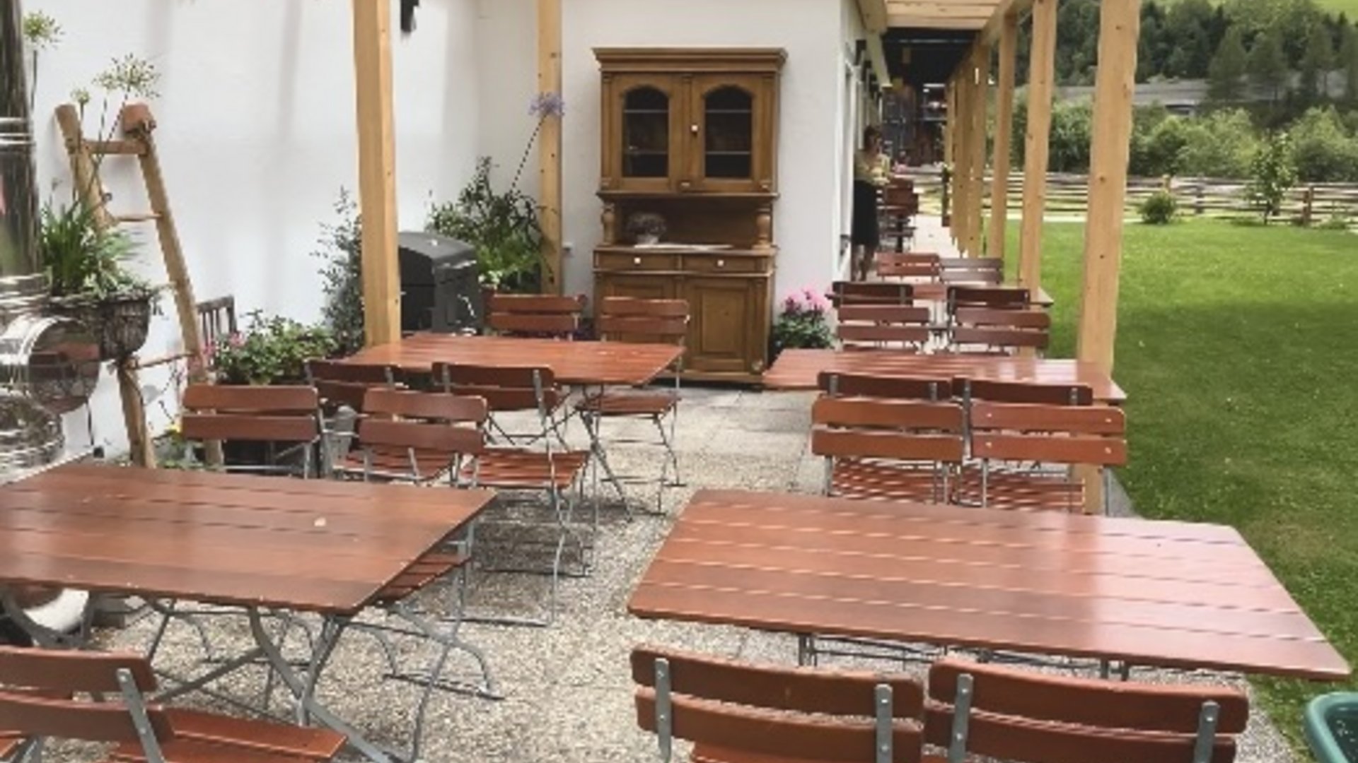 Covered patio with wooden tables and benches next to a lawn