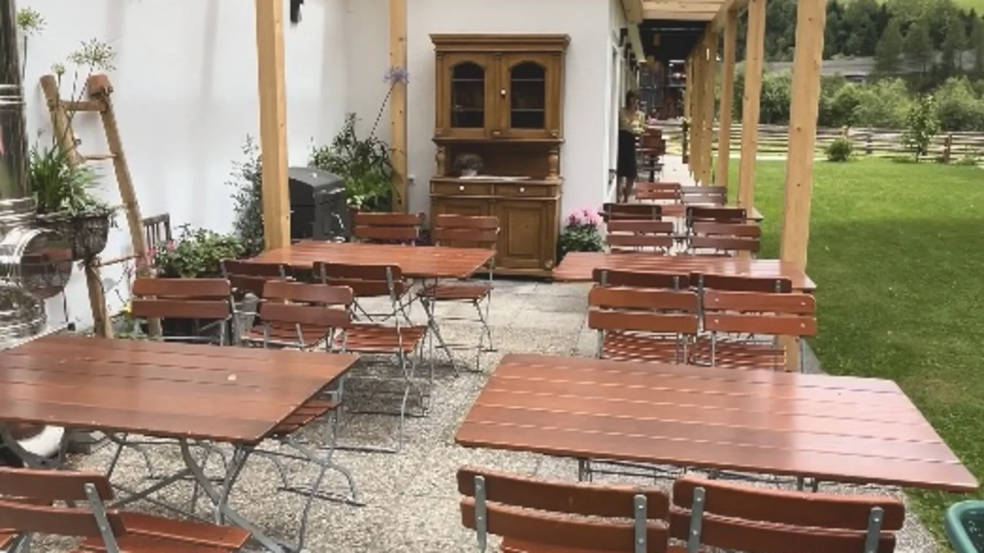 Covered patio with wooden tables and benches next to a lawn