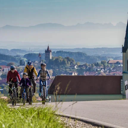 Gezin fietst heuvelopwaarts bij dorp en kerk in glooiend landschap