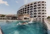 Collective enquiries Person swimming in an outdoor pool in front of a modern building with round windows
