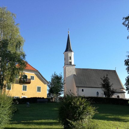 Barocktour © Perwang Kirche Kirche und gelbes Haus auf einem Hügel unter blauem Himmel