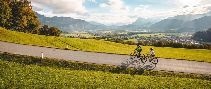 Gasthaus-Hotel Oberwirt **** © Mathäus Gartner Twee fietsers op een weg door groene heuvels met bergen op de achtergrond