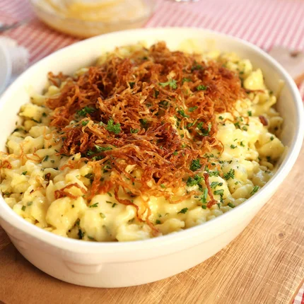 Kaas spaetzle met krokante uitjes en peterselie in een witte ovenschaal