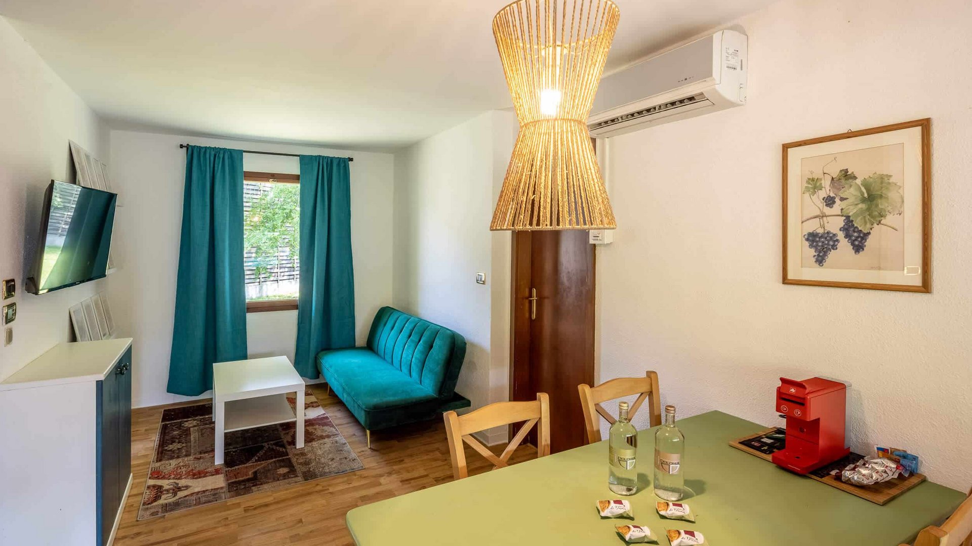 Small living room with green sofa, table, and kitchen area with coffee machine