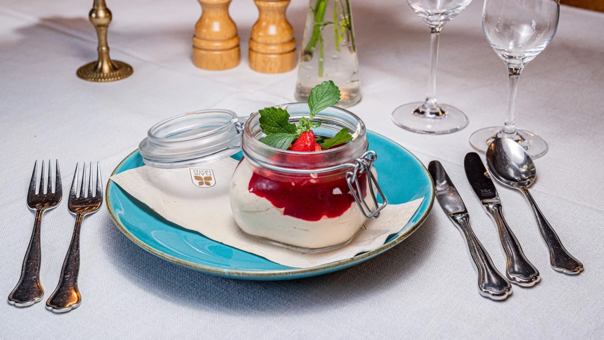 Dessert in glass jar with strawberry sauce and mint on blue plate