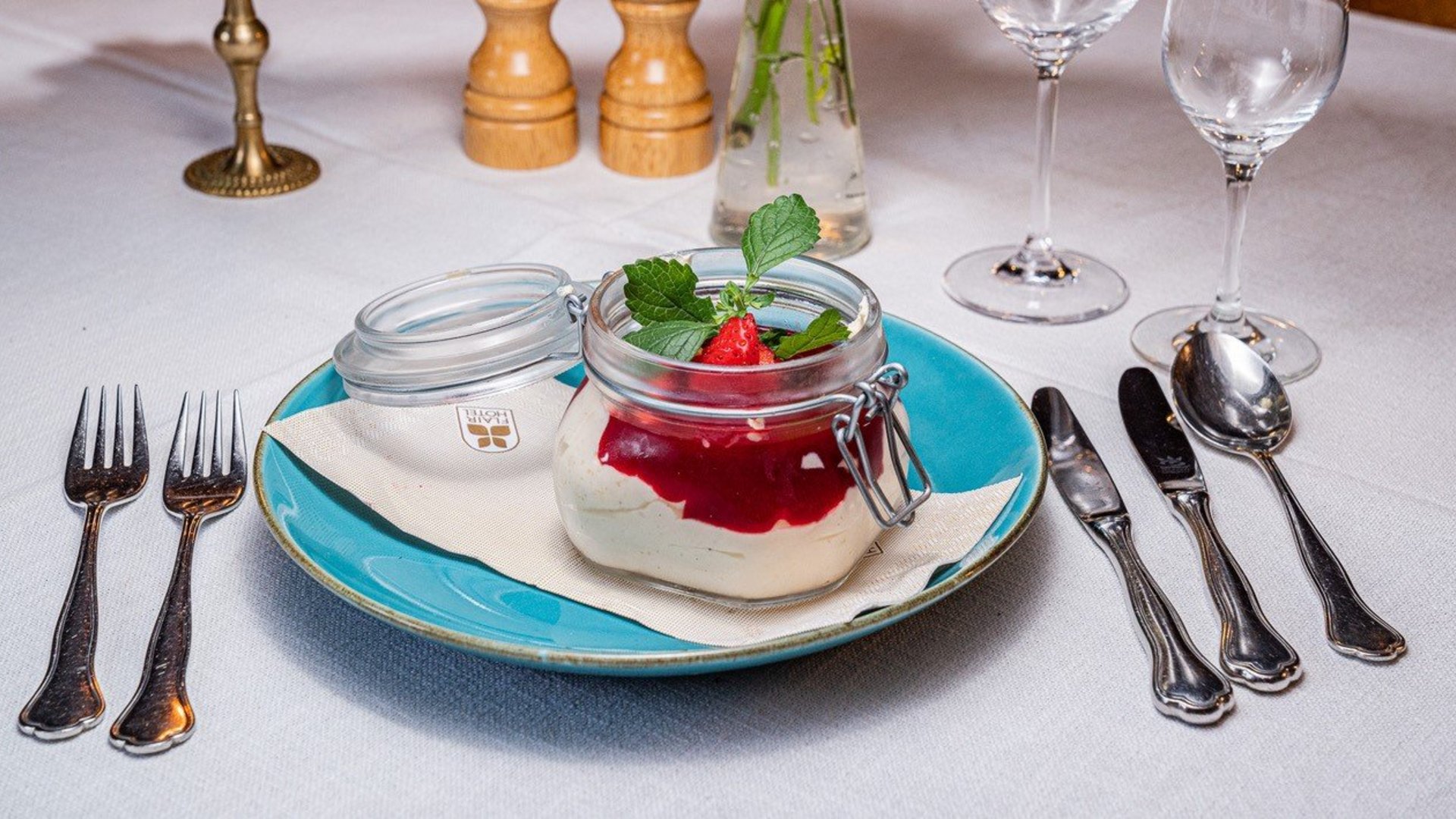 Dessert in glass jar with strawberry sauce and mint on blue plate