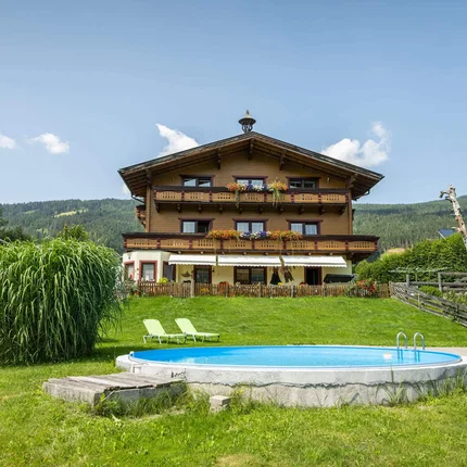 Haus mit Balkon, Garten, Pool und Liegestühlen vor bewaldetem Berg