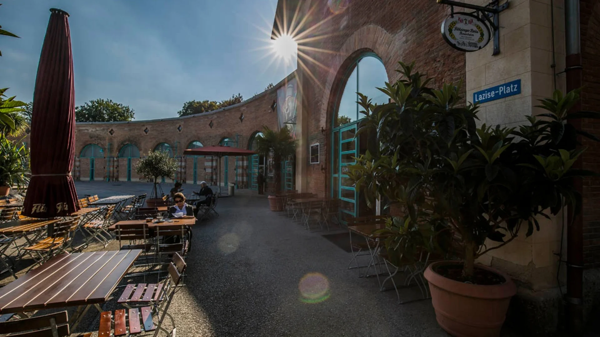 Sonniger Außenbereich eines Cafés mit Tischen, Stühlen und Pflanzen