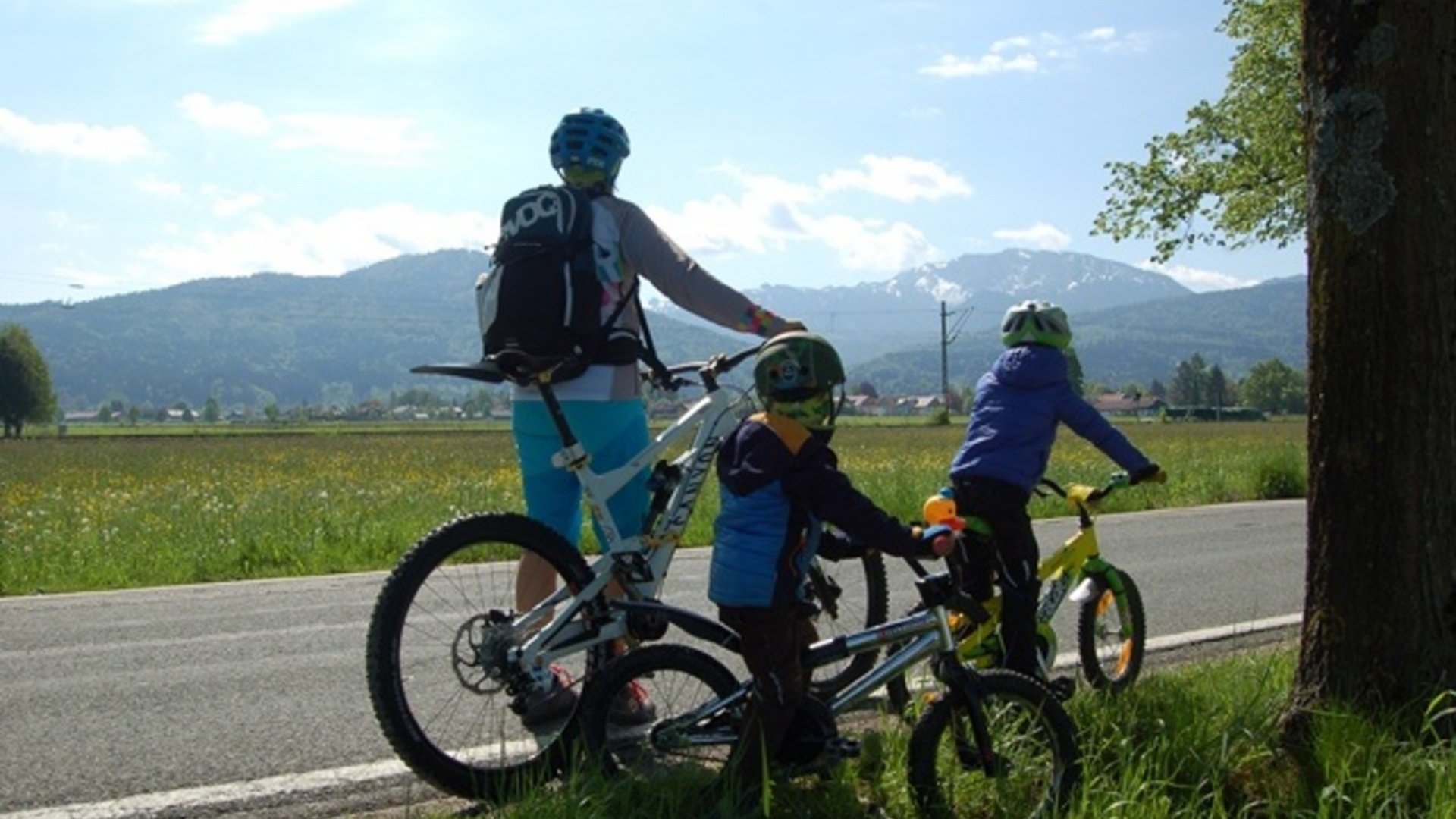 Three cyclists with helmets resting on a country road with mountain view