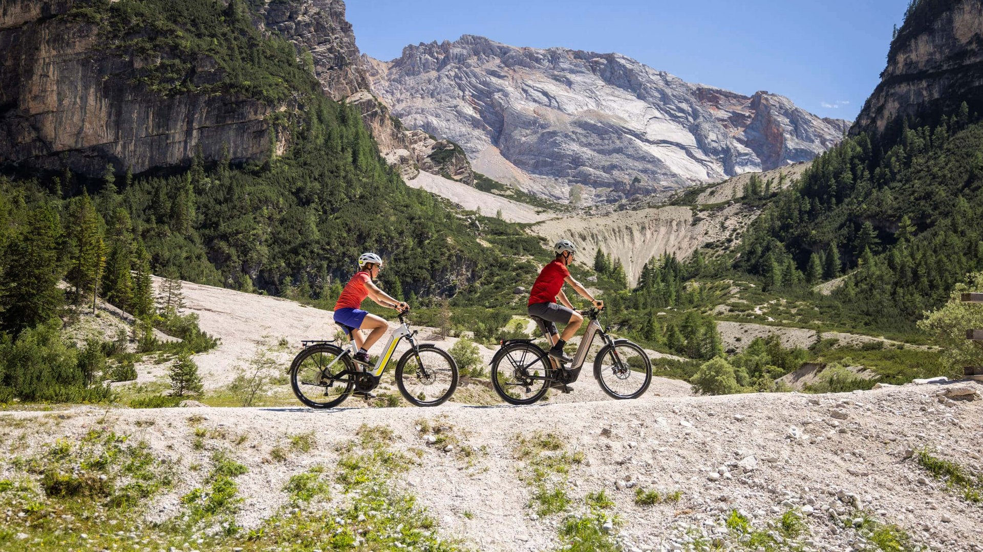 Two people riding e-bikes on a mountain trail in the Alps