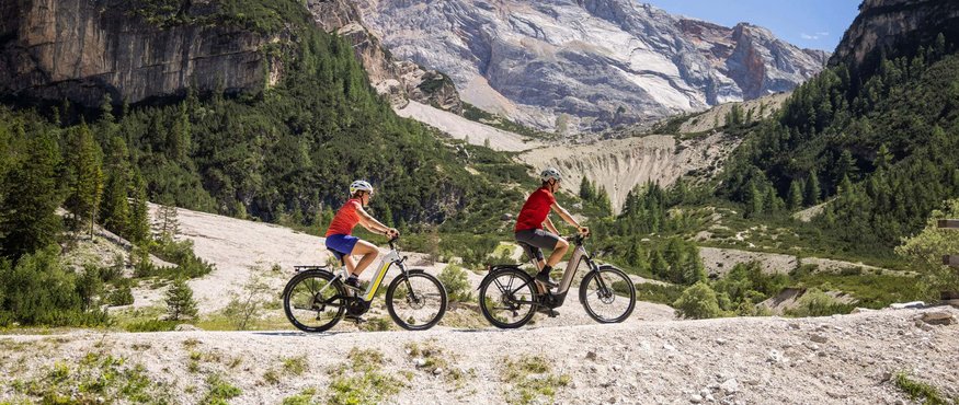 Two people riding e-bikes on a mountain trail in the Alps
