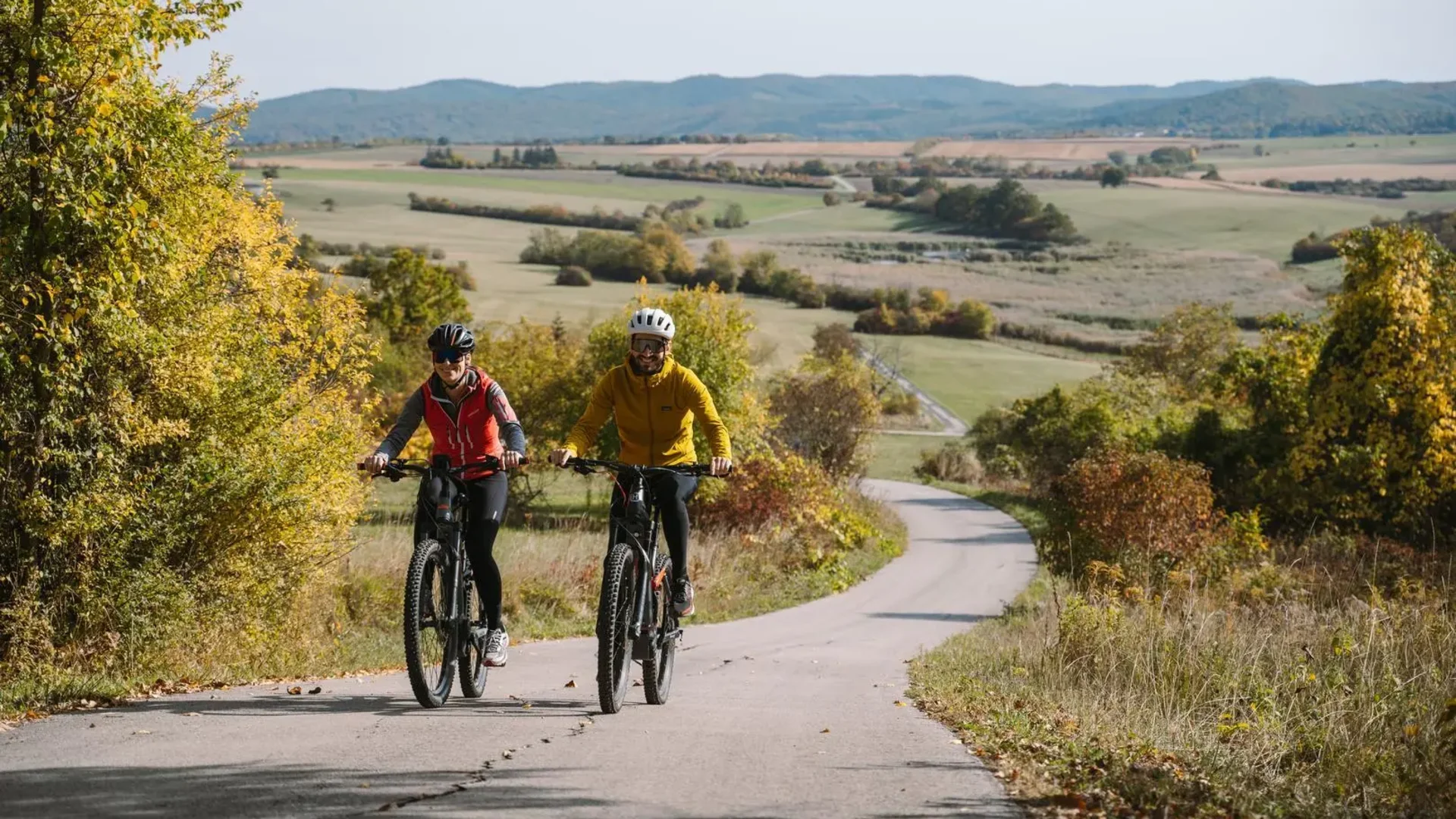 Tour-Detail © Neubauer Zwei Radfahrer auf einem Landweg umgeben von Herbstbäumen und Feldern