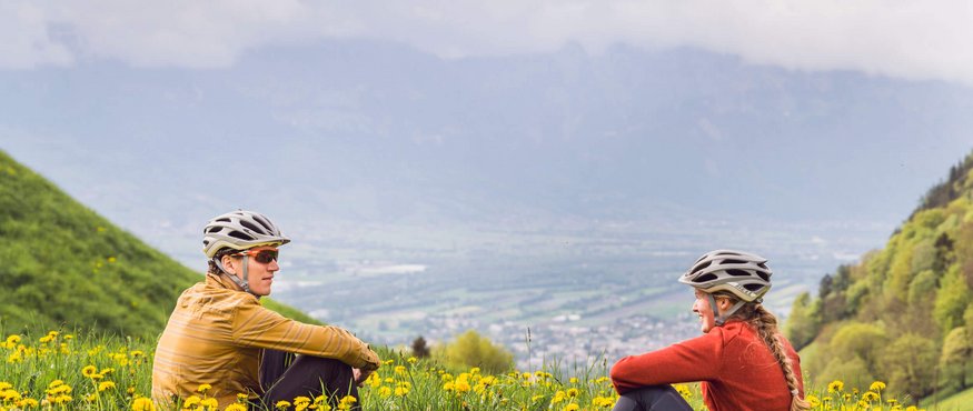 Zwei Radfahrer sitzen im Blumengarten in den Bergen und genießen die Aussicht