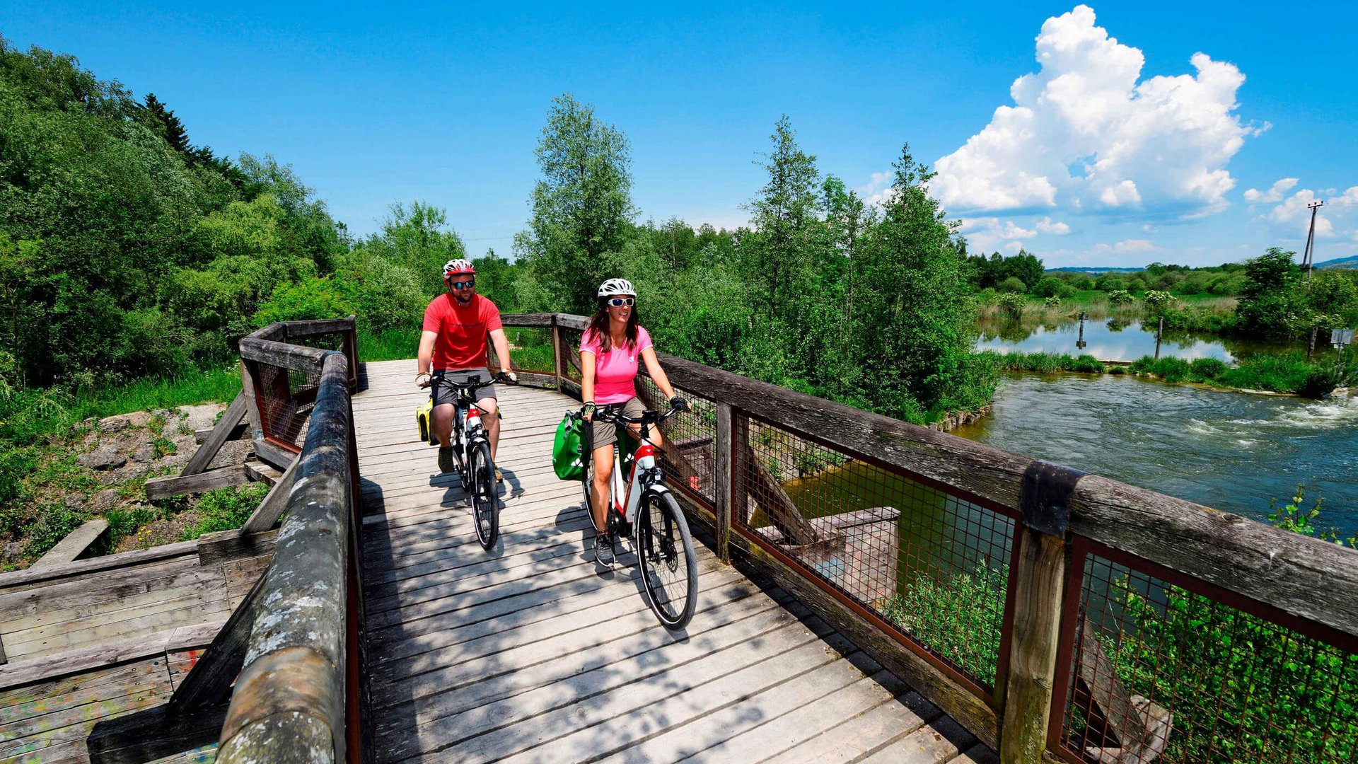Wallersee fietsroute © Salzburger Seenland - Norbert Eisele-Hein Twee fietsers op een houten brug over een rivier bij zonnig weer