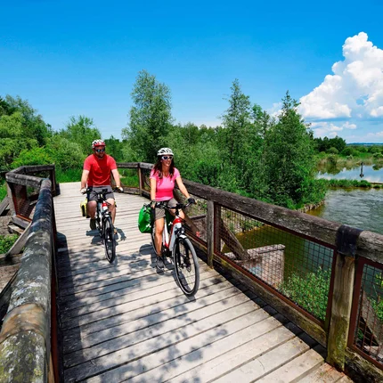 Twee fietsers op een houten brug over een rivier bij zonnig weer
