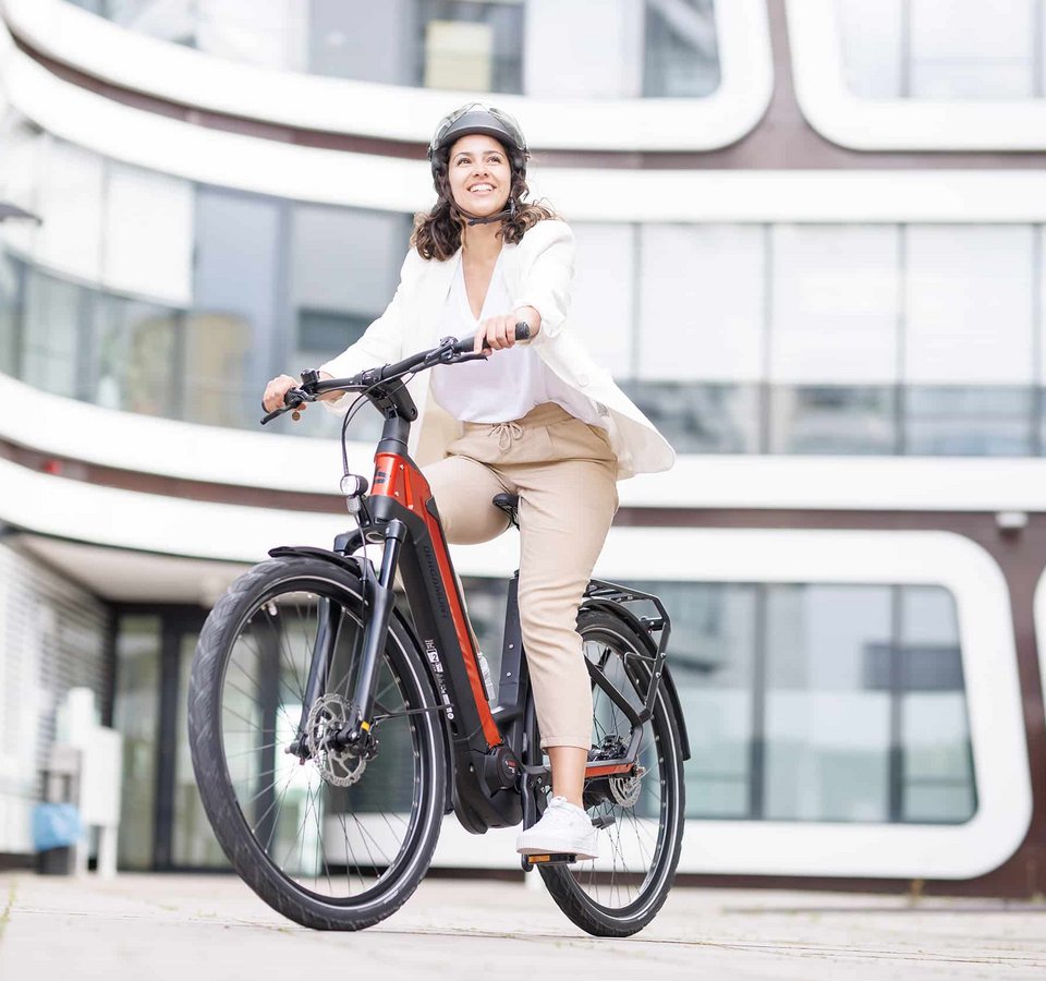 Übertreffe deine Erwartungen © Ralf Bohle GmbH Frau fährt mit Helm ein modernes E-Bike in der Stadt