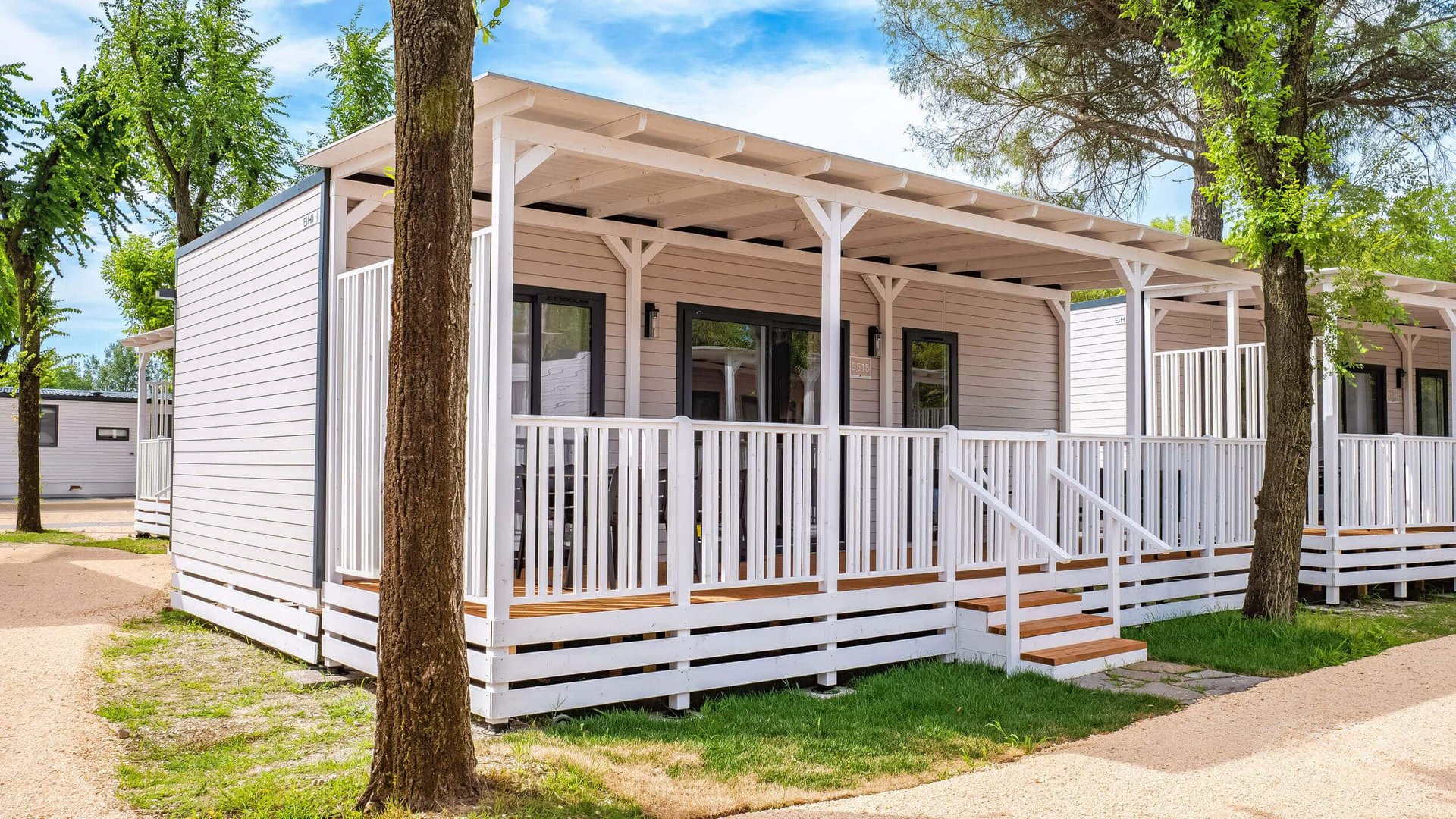 Modern white holiday home with porch surrounded by trees under blue sky