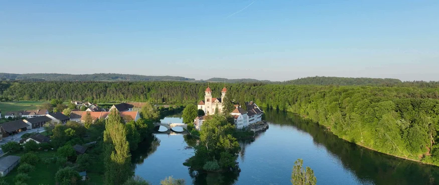 Vier Tage, vier Seiten der RheinWelten © ProWeinland Fluss mit klosterartigem Gebäude auf einer Insel umgeben von Wald und Dorf