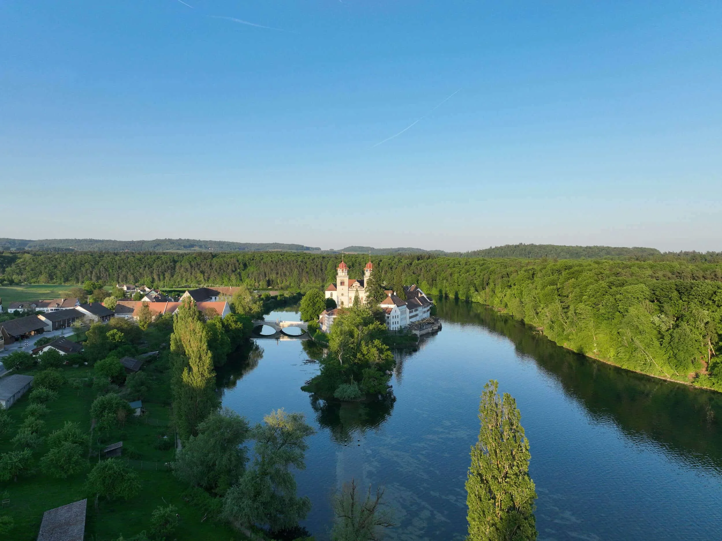 Fluss mit klosterartigem Gebäude auf einer Insel umgeben von Wald und Dorf