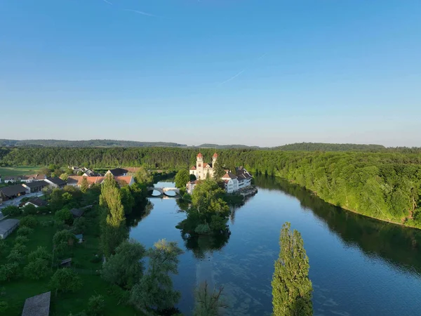 RheinWelten – Eine Reise entlang des Wassers © ProWeinland Fluss mit klosterartigem Gebäude auf einer Insel umgeben von Wald und Dorf