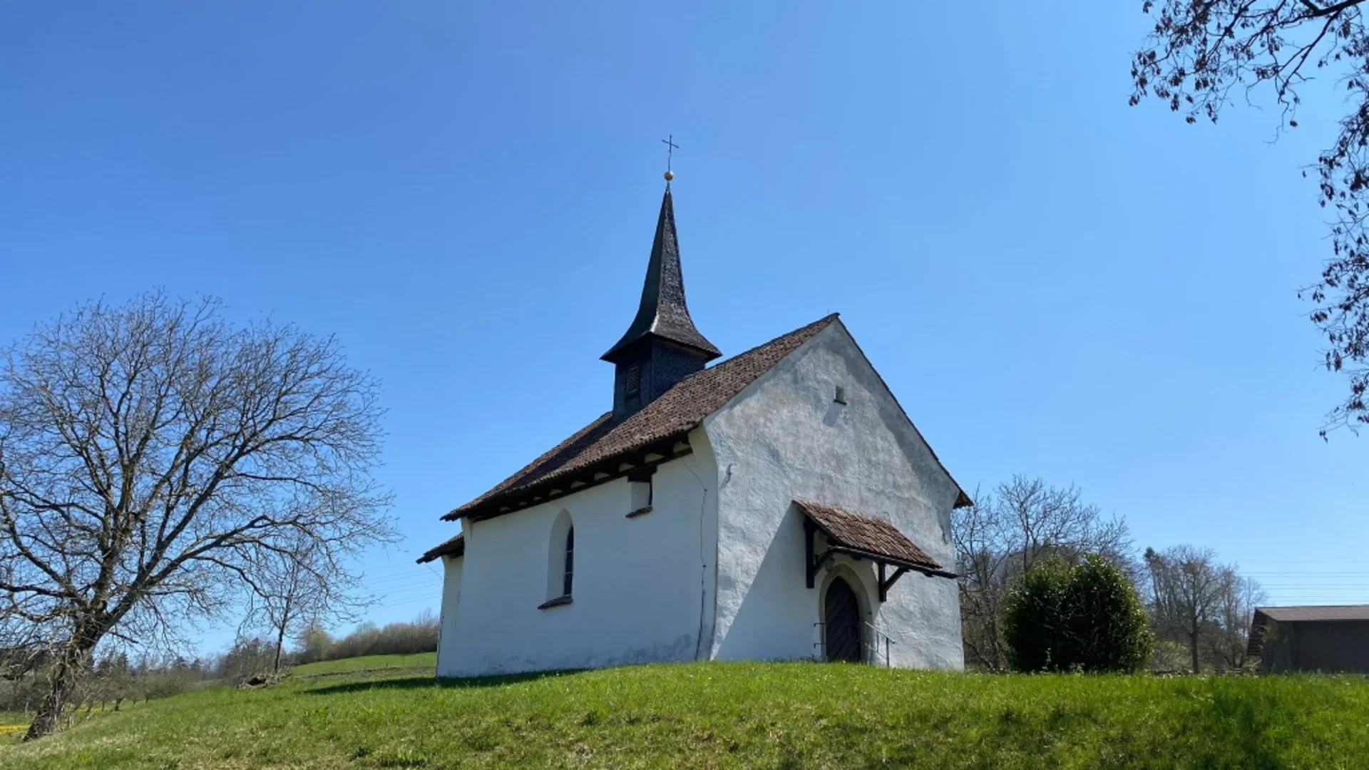 Kleine witte kerk op een groen grasheuveltje onder een blauwe lucht