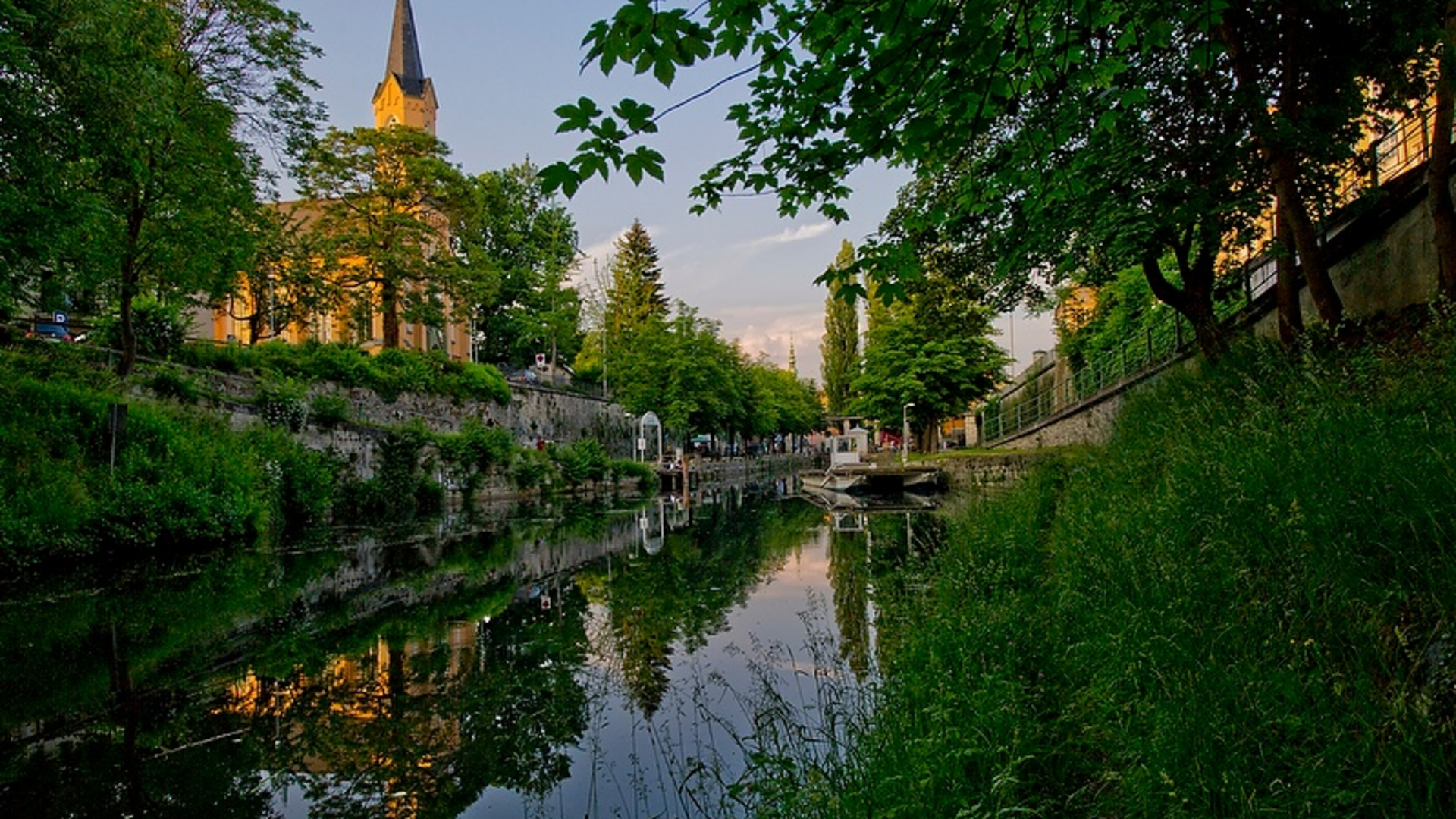 Church by a calm river with green trees and reflection in the water