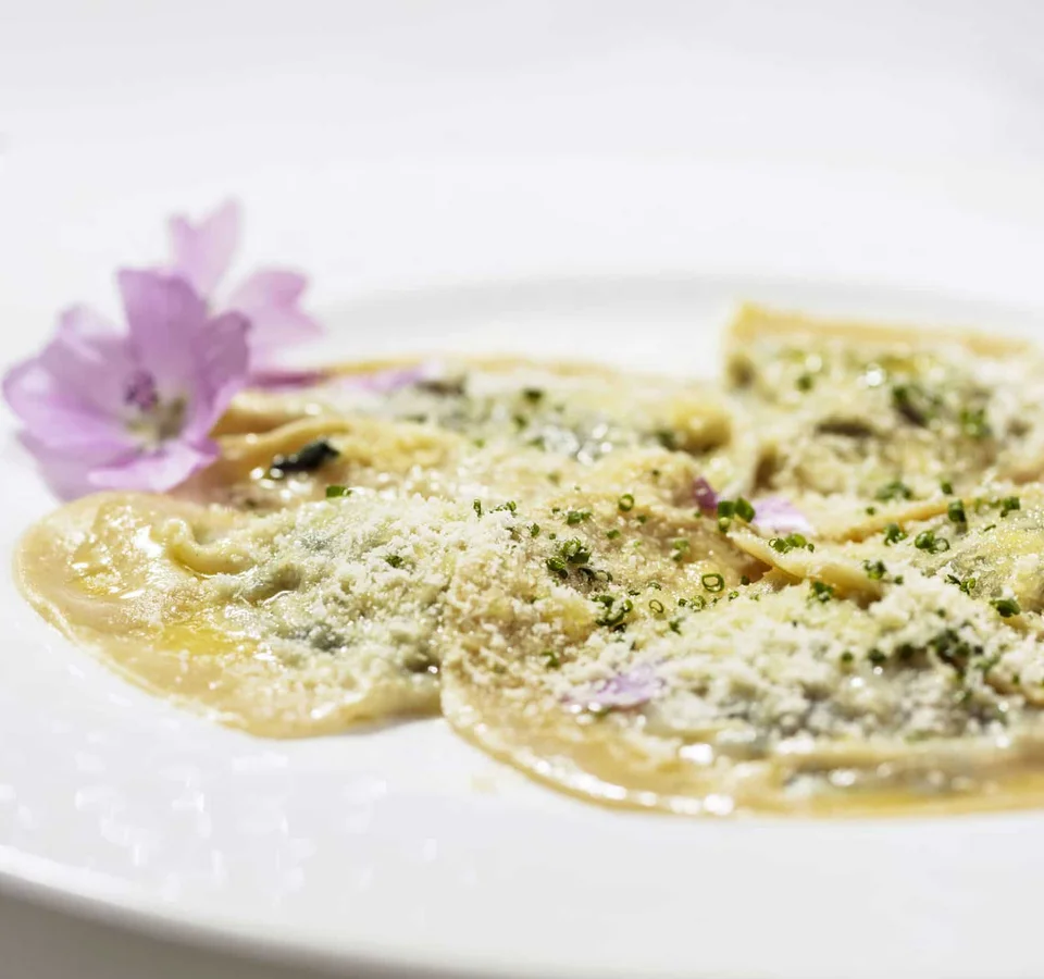Bord met ravioli bestrooid met kaas en gegarneerd met eetbare bloemen