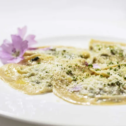Bord met ravioli bestrooid met kaas en gegarneerd met eetbare bloemen