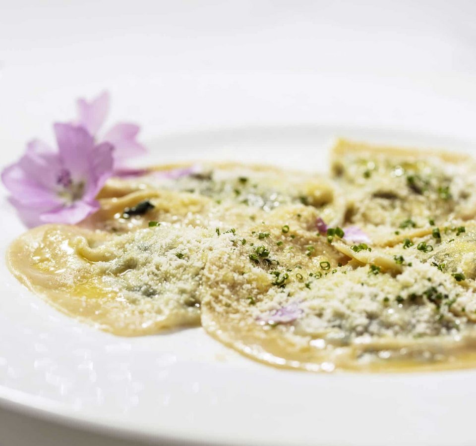 Plate of ravioli sprinkled with cheese and garnished with edible flowers