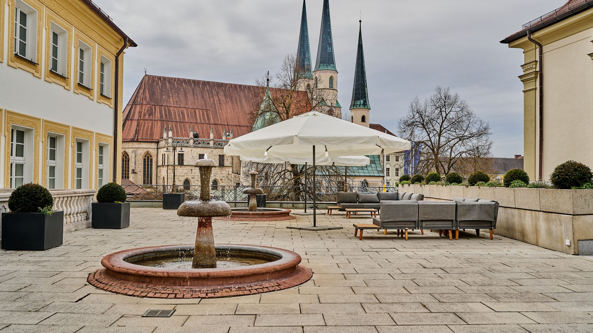 Terrace with fountain and seating area in front of a church with tall spires